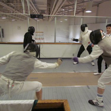 Foil fencers in the foreground and Parviz giving a mini lesson in the background