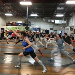 A group of people performing lunges during fencing training